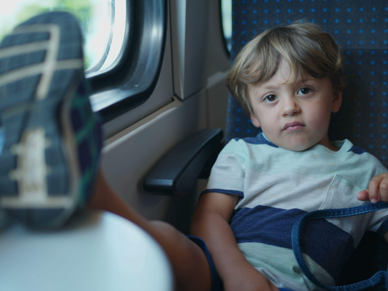 Un niño molesto con los pies sobre la mesa mientras viaja en tren. Niño pequeño travieso que no se comporta bien en un medio de transporte en movimiento