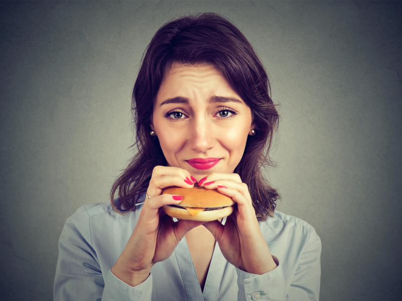 Mujer joven con sentimiento de culpa por comer una hamburguesa