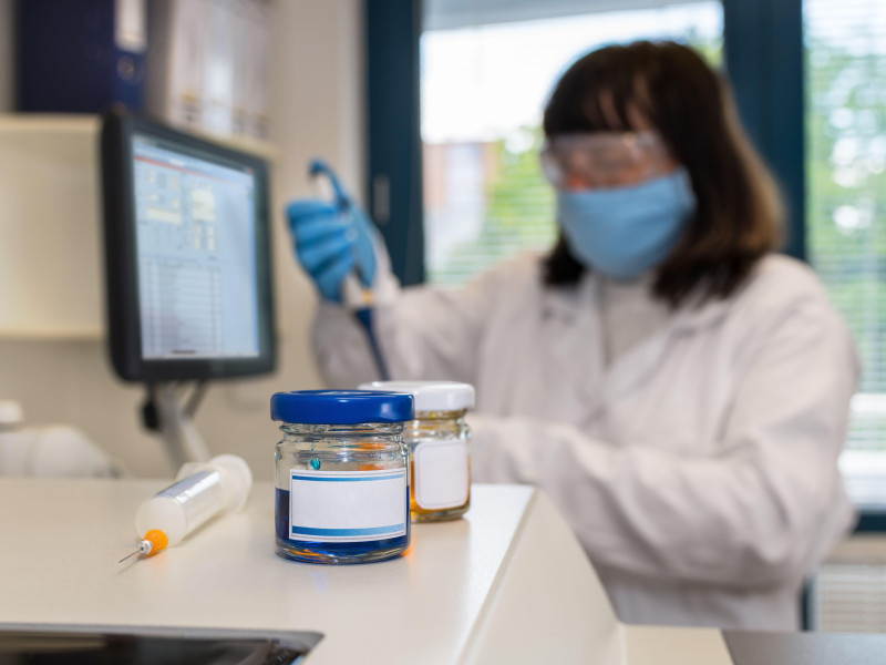 Científica de laboratorio clínico femenina con mascarilla protectora y gafas sosteniendo una pipeta