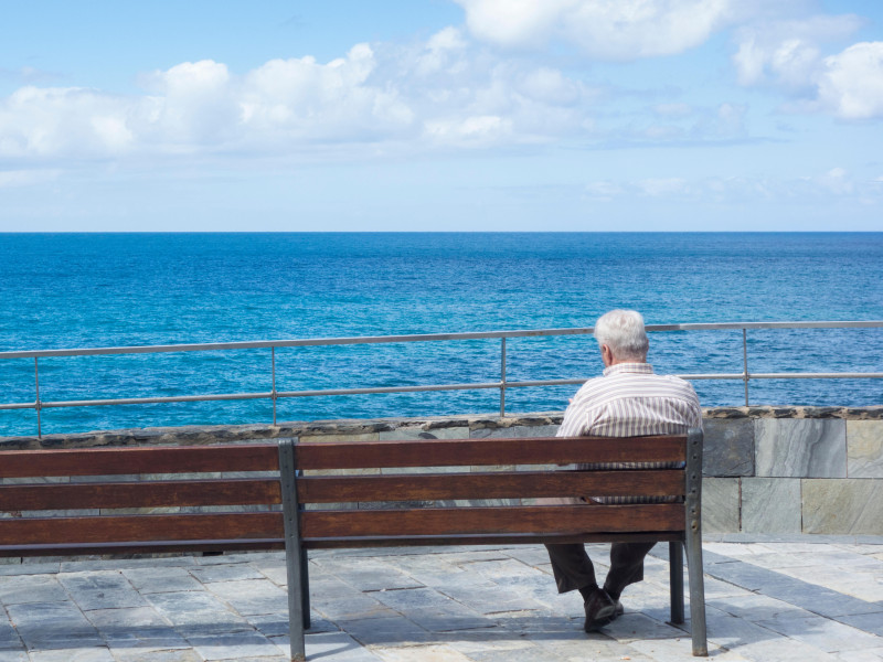 Anciano sentado en un banco mirando al mar en España