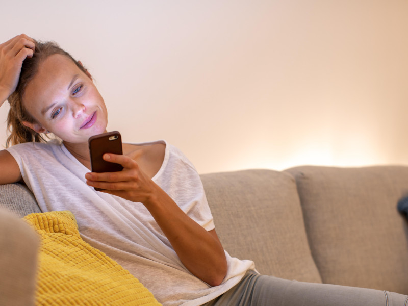 T2E180 Cute young woman on a comfortable sofa in her modern apartment using her cell phone