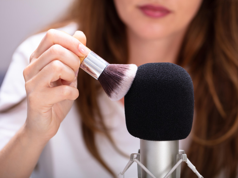 Mujer usando un pincel sobre un micrófono para hacer sonidos ASMR