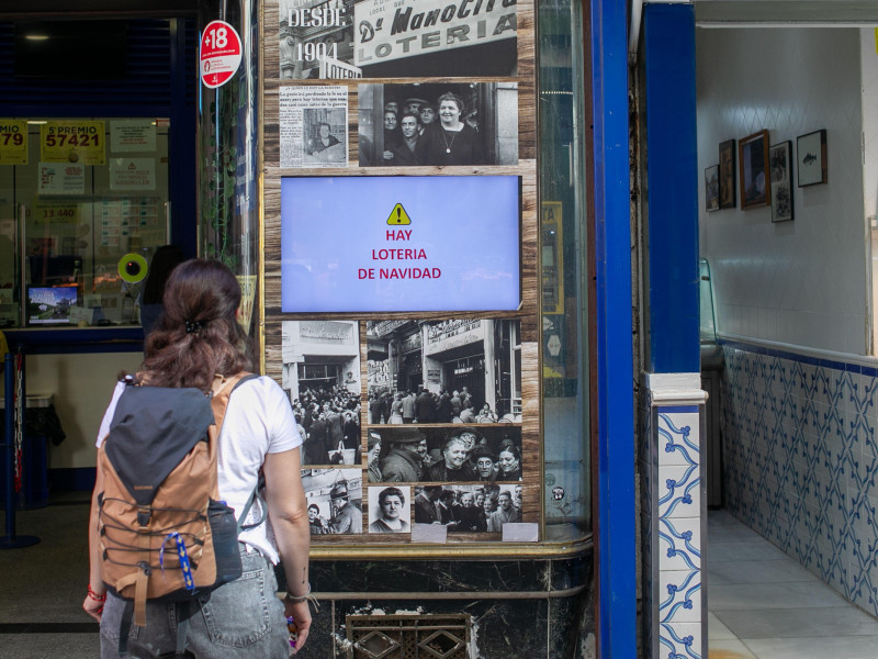 Una mujer lee un cartel que indica la venta de billetes de lotería de Navidad a la entrada de la oficina de loterías de Doña Manolita en Madrid