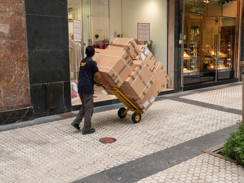 Repartidor en la calle con un montón de cajas en un carrito de mano. No puede ver hacia adelante para ver los paquetes. San Sebastián, España