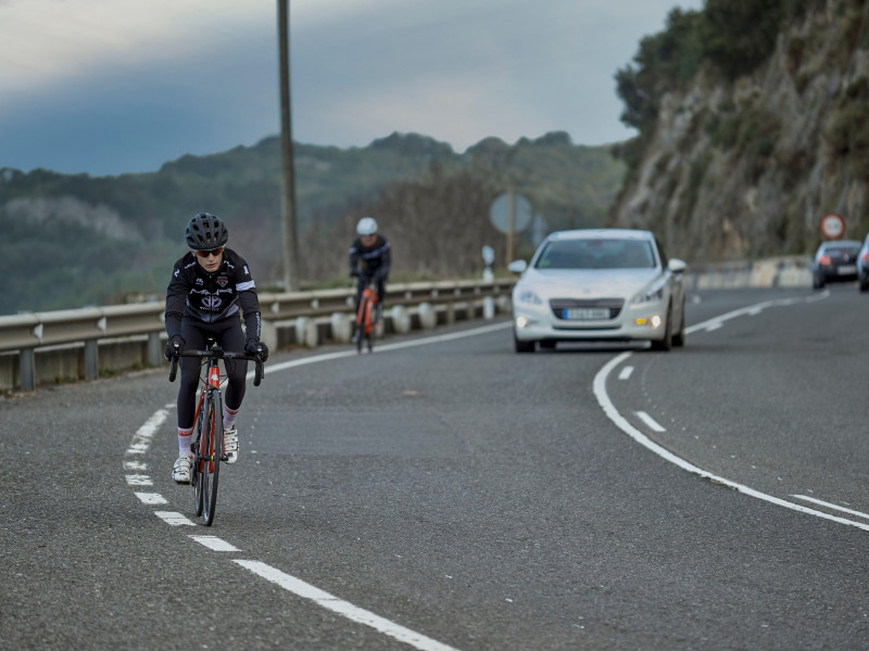 Un coche adelanta a dos ciclistas en una curva de la carretera de Islares, Cantabria, España