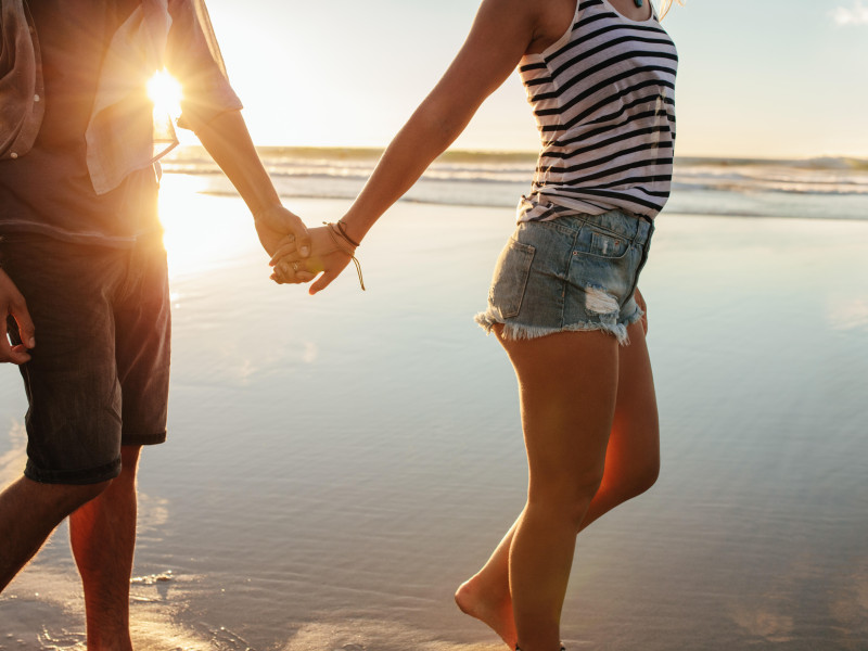 Fotografía recortada de una pareja joven tomada de la mano y caminando por la playa. Un hombre y una mujer enamorados paseando por la orilla