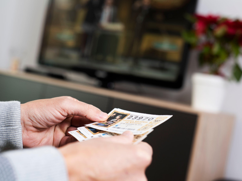 Primer plano de un hombre con algunos billetes de la Lotería de Navidad española en la mano mientras ve la emisión televisada