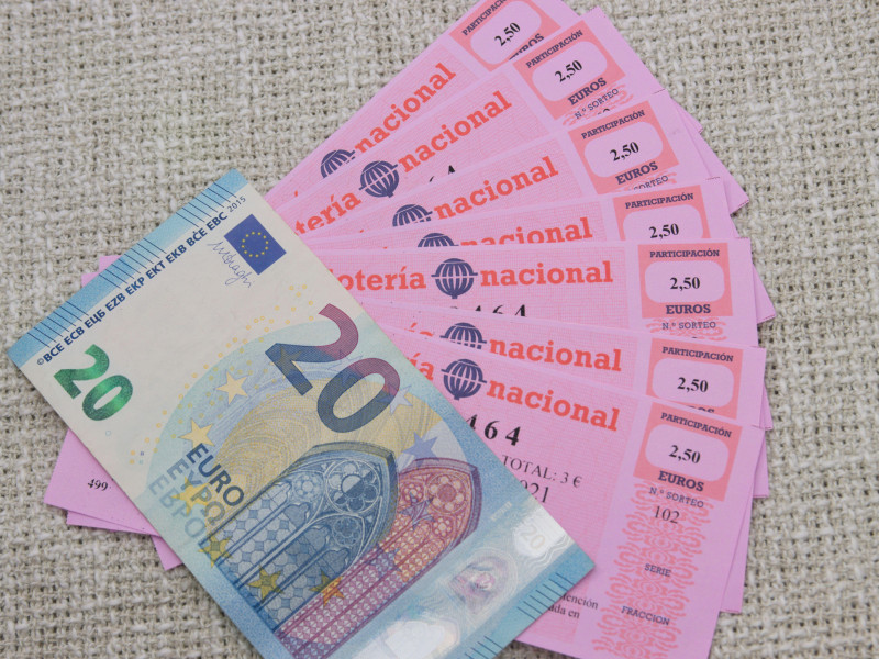 Participaciones equivalentes a un boleto de lotería nacional española por valor de 20€ junto con un billete de 20€ sobre fondo neutro