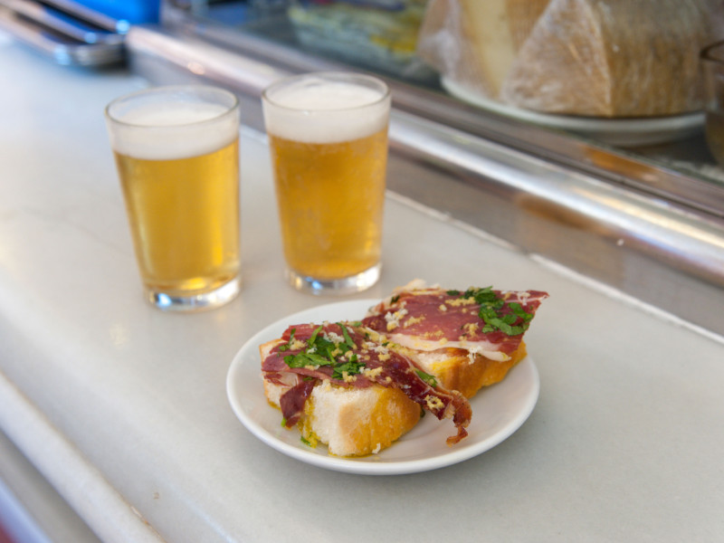 Primer plano de tapas de jamón serrano y cervezas en la barra del bar