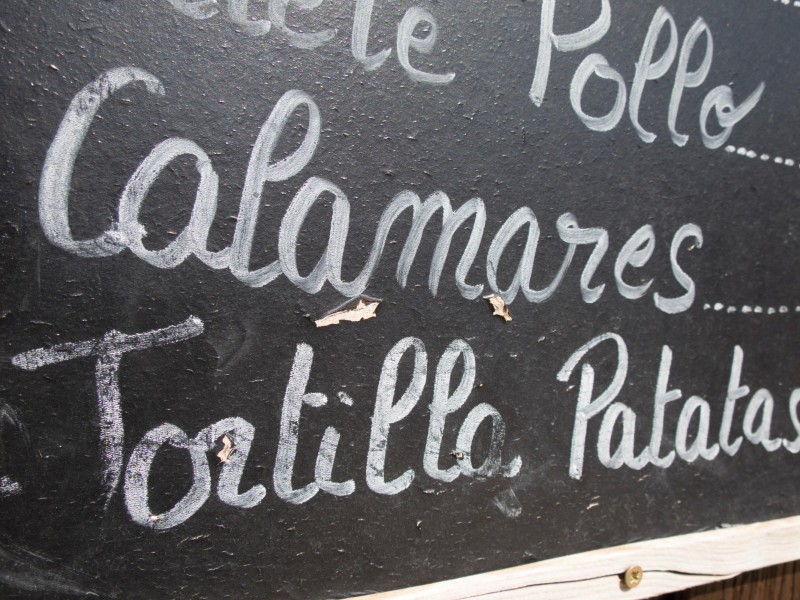 Cartel negro escrito a mano en español en la pared con menú de platos típicos de comida de restaurante español como calamares y tortilla de patatas