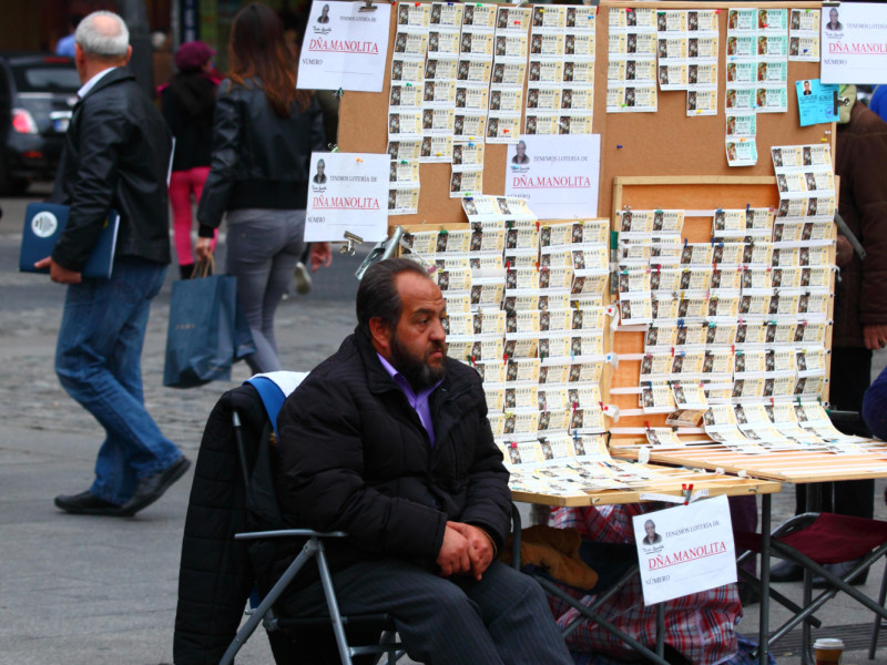 Un hombre se sienta junto a su puesto de venta de billetes de la Lotería de Navidad en la Plaza Puerta del Sol, en el centro de Madrid