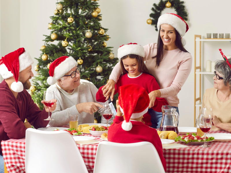 Feliz y sonriente madre e hija cortando pavo en el almuerzo familiar de Navidad en casa