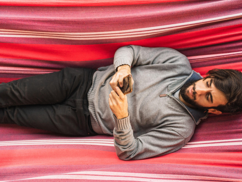 Hombre hipster usando un teléfono móvil en una hamaca