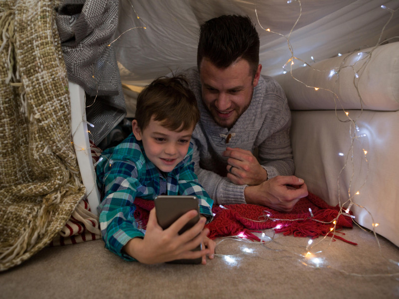 Padre e hijo usando un teléfono móvil en el dormitorio