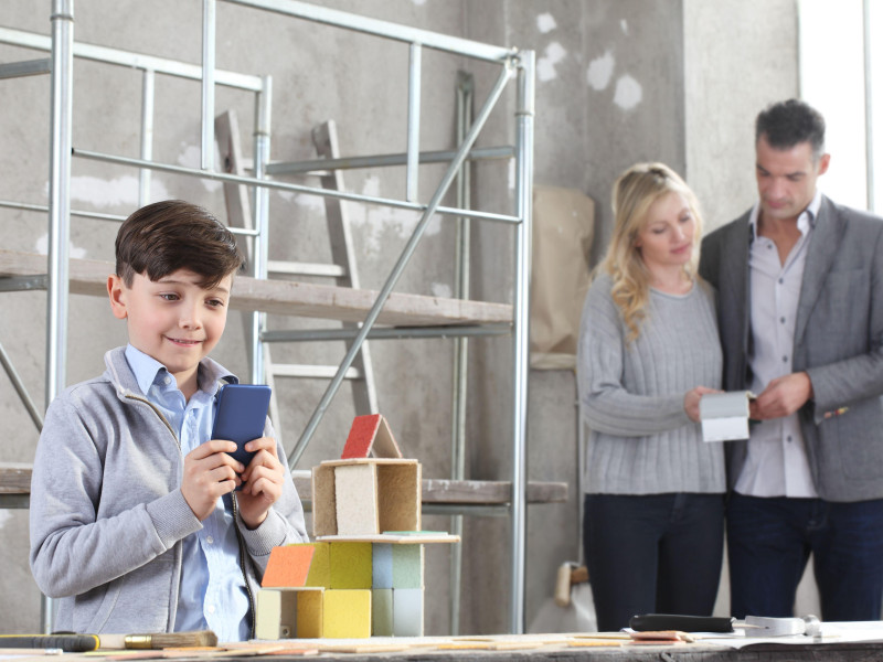 Niños felices con el teléfono móvil jugando a construir una casa con modelos de construcción