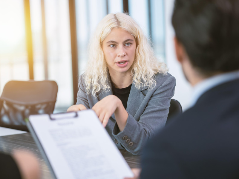 Mujer de negocios joven con ojos enfocados y segura habla atentamente con su jefe en la sala de reuniones de la oficina para una entrevista de trabajo