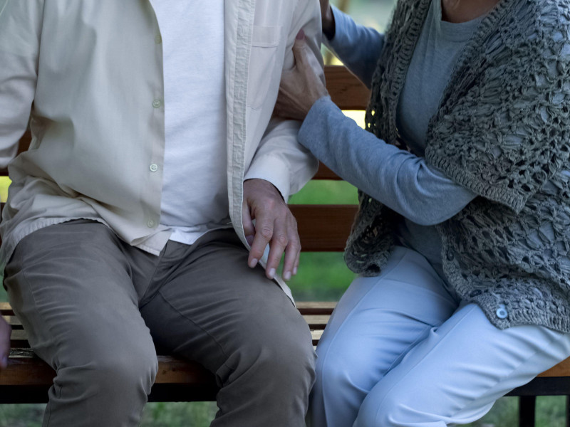 Mujer apoyando a un viejo amigo enfermo, sentada en un parque del hospital, enfermedad de Parkinson