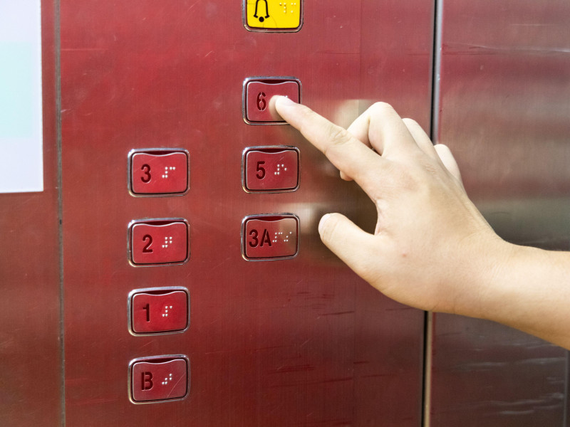 Persona ciega leyendo braille con el dedo en el panel del ascensor