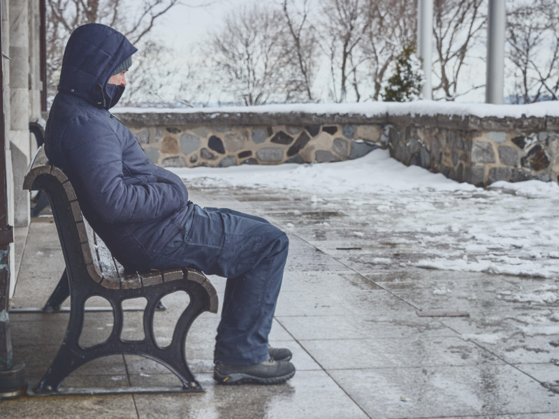 Hombre sentado en un banco en invierno con nieve en el suelo