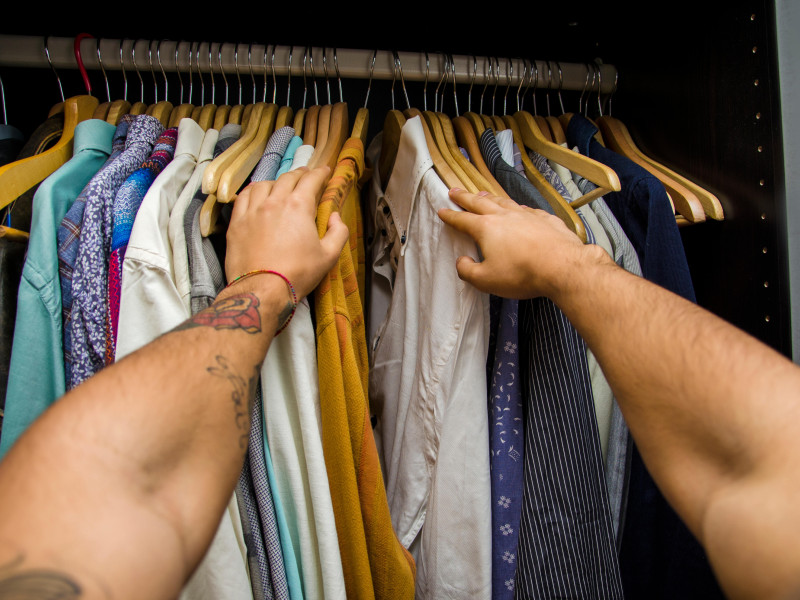 Hombre buscando una camisa colgada en la barra de su armario, vista en primera persona mirando hacia abajo desde sus brazos