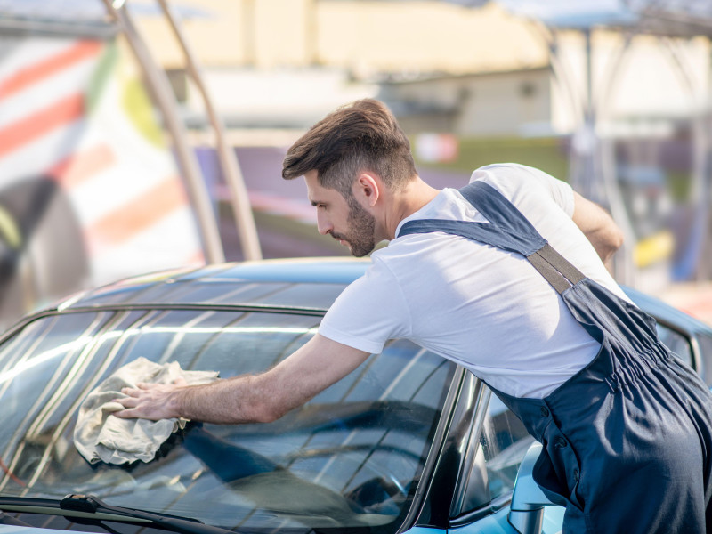 Hombre con camisa y mono limpiando el cristal del coche