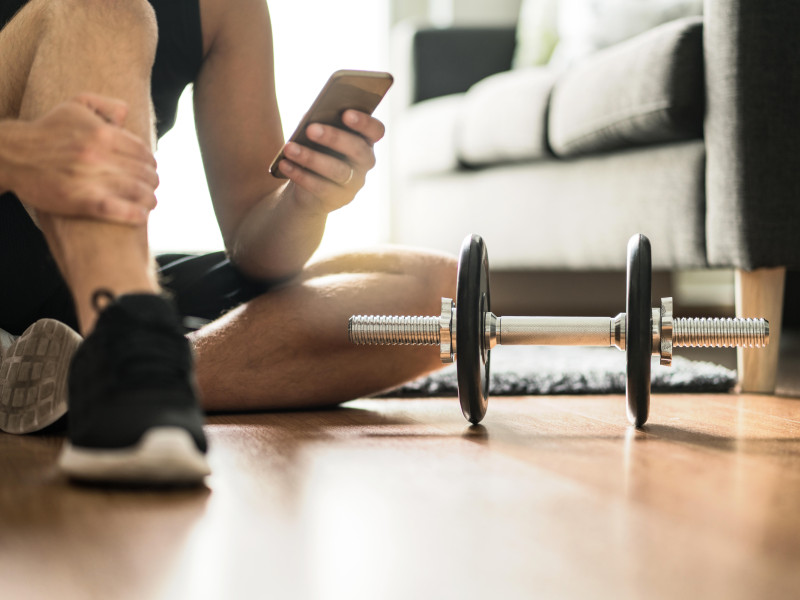 Hombre usando un teléfono inteligente mientras hace ejercicio en casa