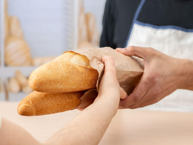 Fotografía recortada de una mujer comprando baguettes o pan recién hechos en una cafetería