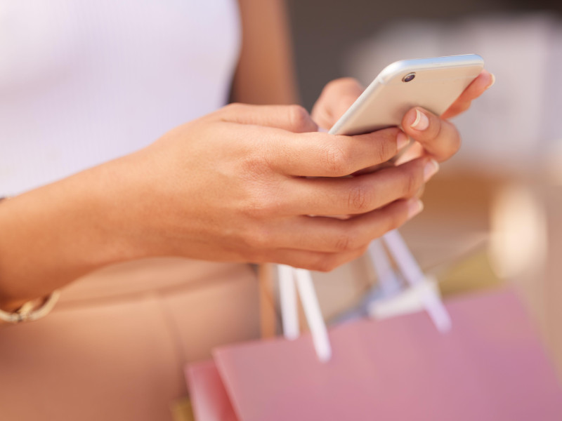 Manos con smartphone, mujer y bolsa de compras en un centro comercial para terapia de compras con tecnología y comunicación. Aplicación móvil, zoom de teléfono y compras