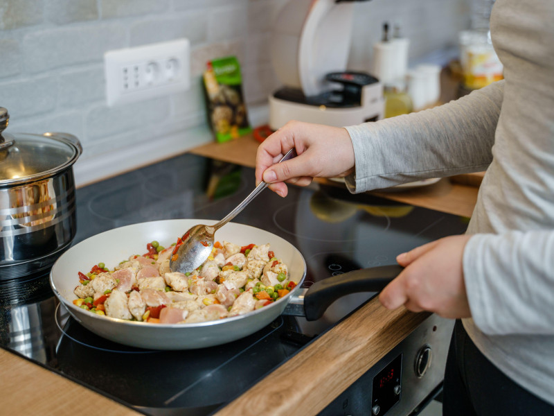 Vista lateral de una mujer caucásica desconocida con una sartén preparando una comida saludable vegana o vegetariana en casa