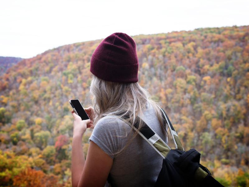 Vista trasera de una mujer joven usando un teléfono mientras está de pie frente a una montaña