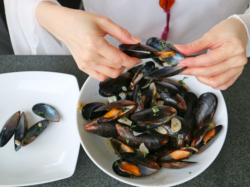 Preparar mejillones al vapor en un plato de vino blanco utilizando una concha de mejillón vacía para extraer la carne de otro mejillón