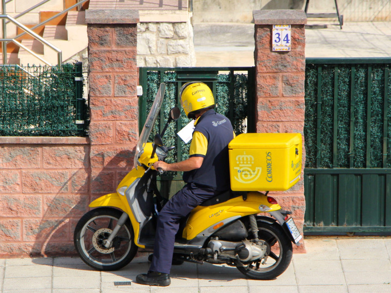 Cartero de Correos repartiendo correo desde una moto amarilla en Santander, Cantabria