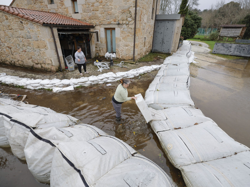 Los vecinos ayudan a los propietarios a limpiar una casa de Turismo Rural, anegada a pesar de las barreras que situaron a su alrededor, hoy en Lamas, Padrón, A Coruña