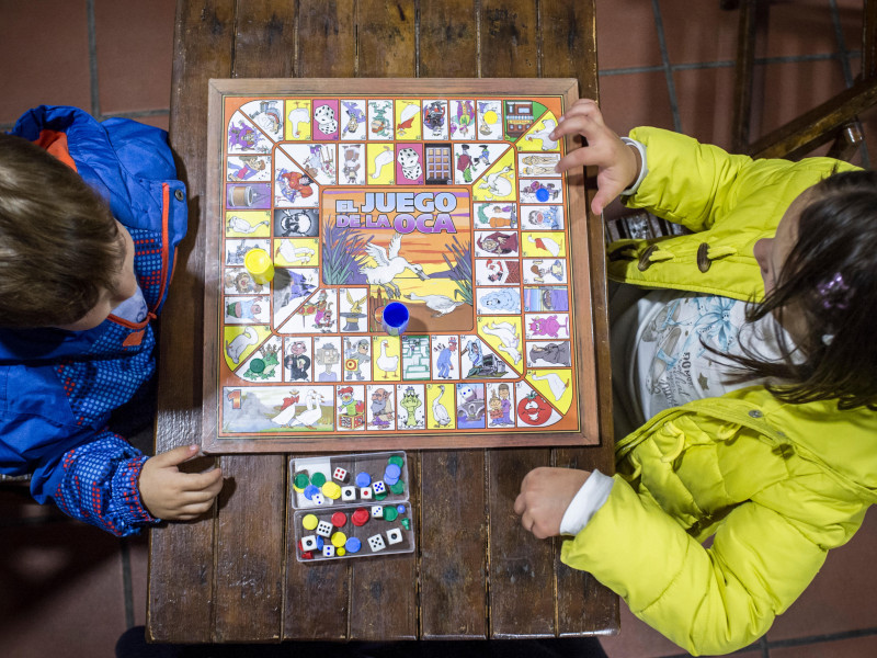 Hermanos pequeños jugando al Juego de la Oca sobre una mesa de madera antigua. Vista aérea. Juego de mesa tradicional