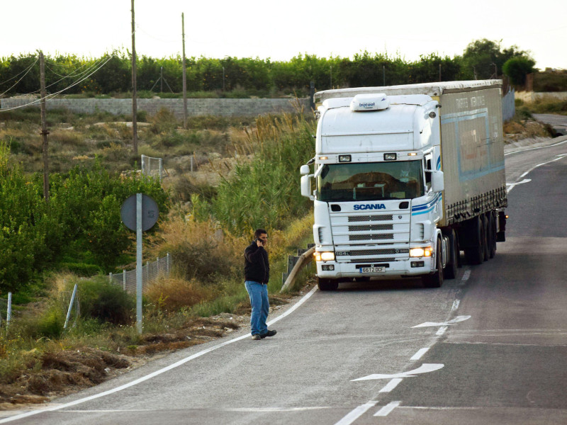 Hombre hablando por teléfono a punto de ser atropellado por un camión. Posible colisión en la carretera. Muerte inminente o accidente.