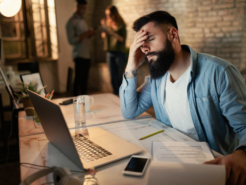 Exhausted businessman holding his head in pain while working late in the office.