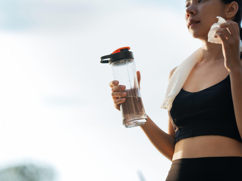 Una hermosa joven asiática se detiene para beber agua y secarse el sudor después de su carrera vespertina en el parque