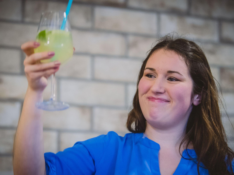 Una joven caucásica con cabello castaño está animando o celebrando con un vaso de gin tonic en la mano