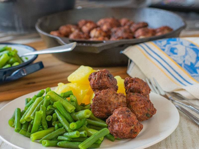 Comida casera recién hecha con albóndigas fritas, judías verdes y patatas hervidas servidas en un plato con una sartén de fondo en la mesa de la cocina