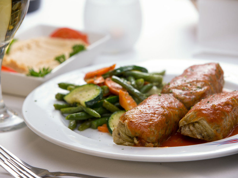 Rollos de pavo servidos con judías verdes al vapor, zanahorias y calabacines, complementados con un plato de hummus.