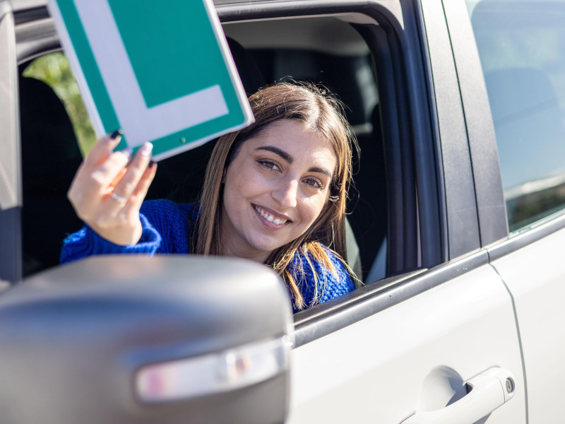 Feliz joven conductora mostrando su L tras pasar por la autoescuela en España