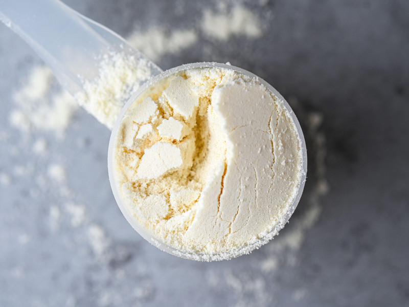 Vista superior de una cucharada de nutrición deportiva, proteínas, creatina y ganador en forma de polvo blanco sobre fondo gris