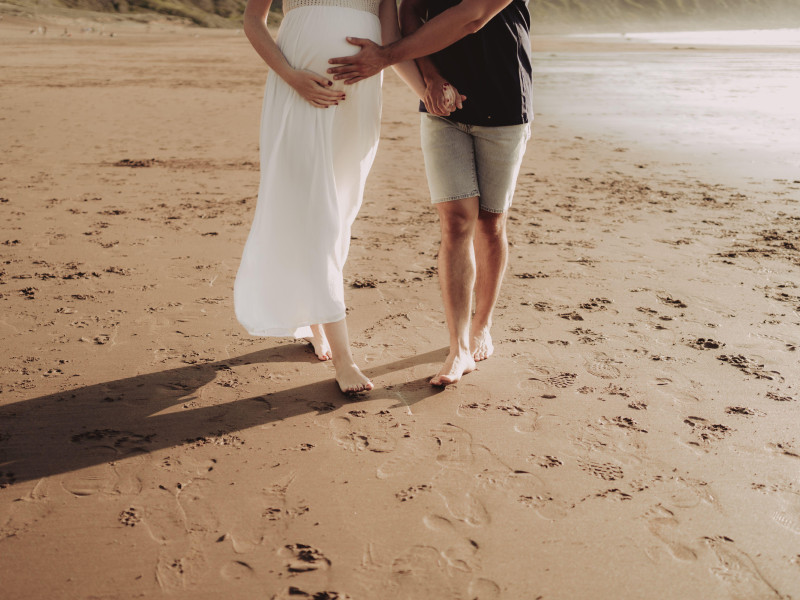 Una hermosa mujer embarazada y su pareja caminando por una playa de arena en el País Vasco, España