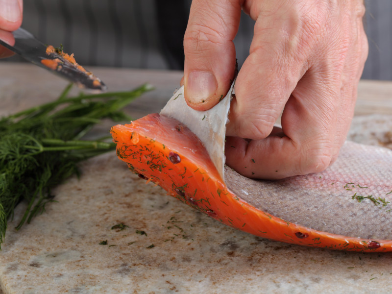 Cocine quitando la piel del filete de salmón salado en una tabla de cortar