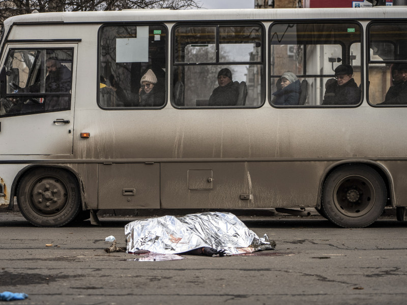 Los pasajeros de un autobús observan el cuerpo de una mujer tendido en la calle cubierto con una manta tras un bombardeo en el centro de Donetsk, Ucrania controlada por Rusia, el 20 de febrero de 2024