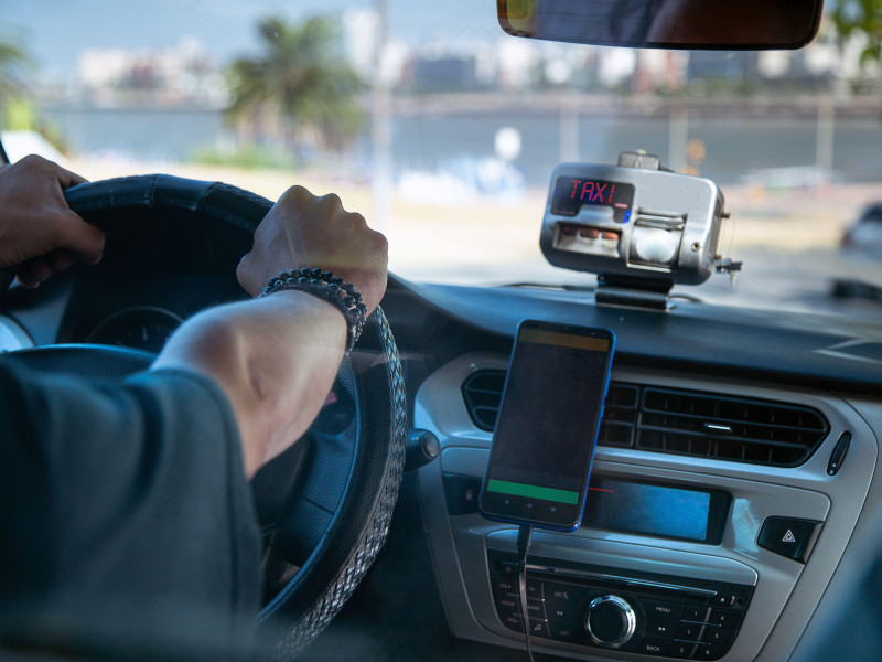 Conductor de taxi conduciendo un coche con taxímetro y teléfono inteligente montado en el salpicadero