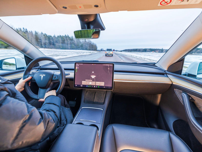 Una mujer conduce un Tesla Model Y en una autopista invernal con una pantalla táctil que muestra datos del vehículo y el entorno