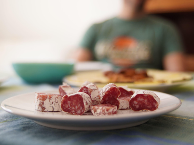 Imagen de cubos de fuet típicos españoles cortados en cubitos en un plato blanco en una comida de amigos con queso desenfocado y una figura humana en el fondo