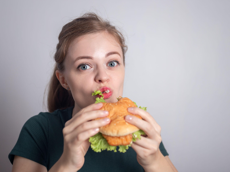 Mujer caucásica joven sonriente sosteniendo una hamburguesa de pollo para comer