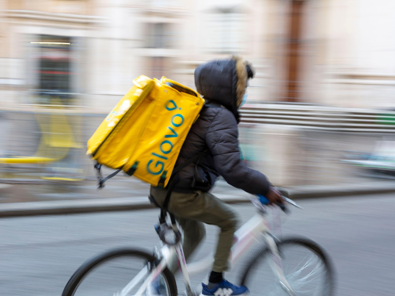 Fotografía borrosa con movimiento de un repartidor de comida en bicicleta con una caja térmica amarilla de Glovo